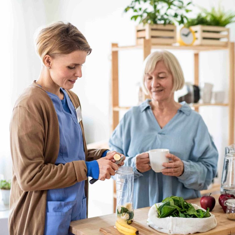 Senior woman with caregiver or healthcare worker indoors, preparing food. Happy senior woman with caregiver or healthcare worker indoors, preparing food.