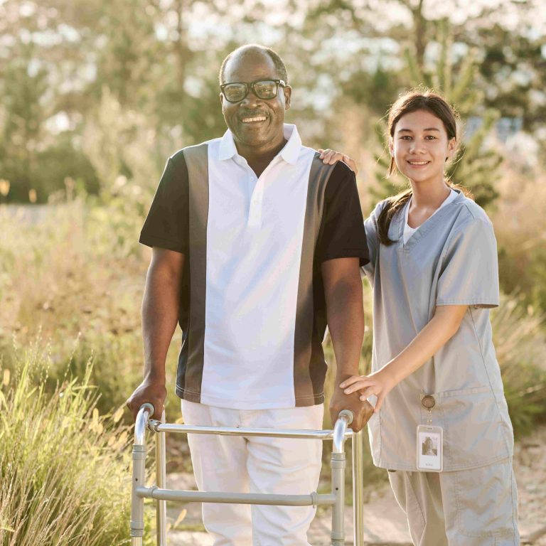 Portrait of African American senior man smiling at camera while walking outdoors with nurse