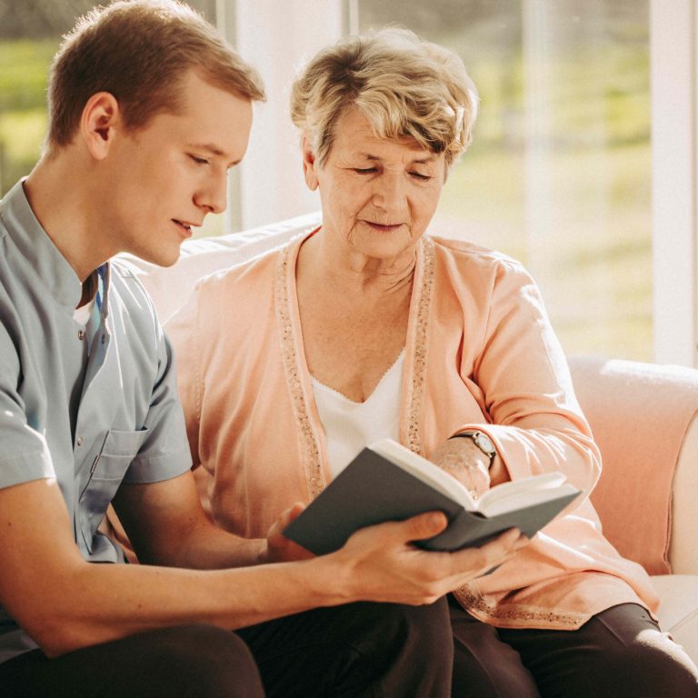 Young male nurse reading a book to an older woman