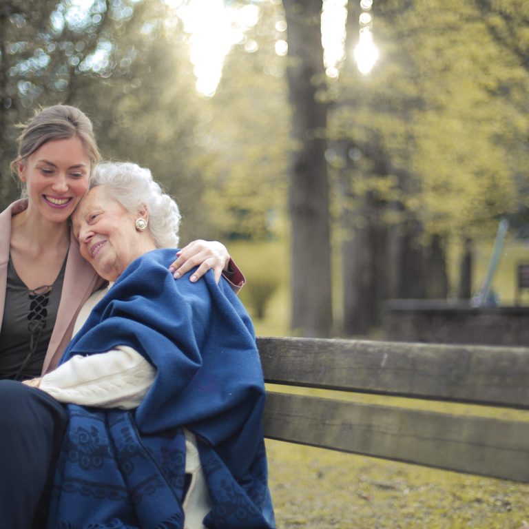 Granddaughter sitting on a bench in a park with her grandmother and hugging her A granddaughter sitting on a bench in a park with her grandmother and hugging her